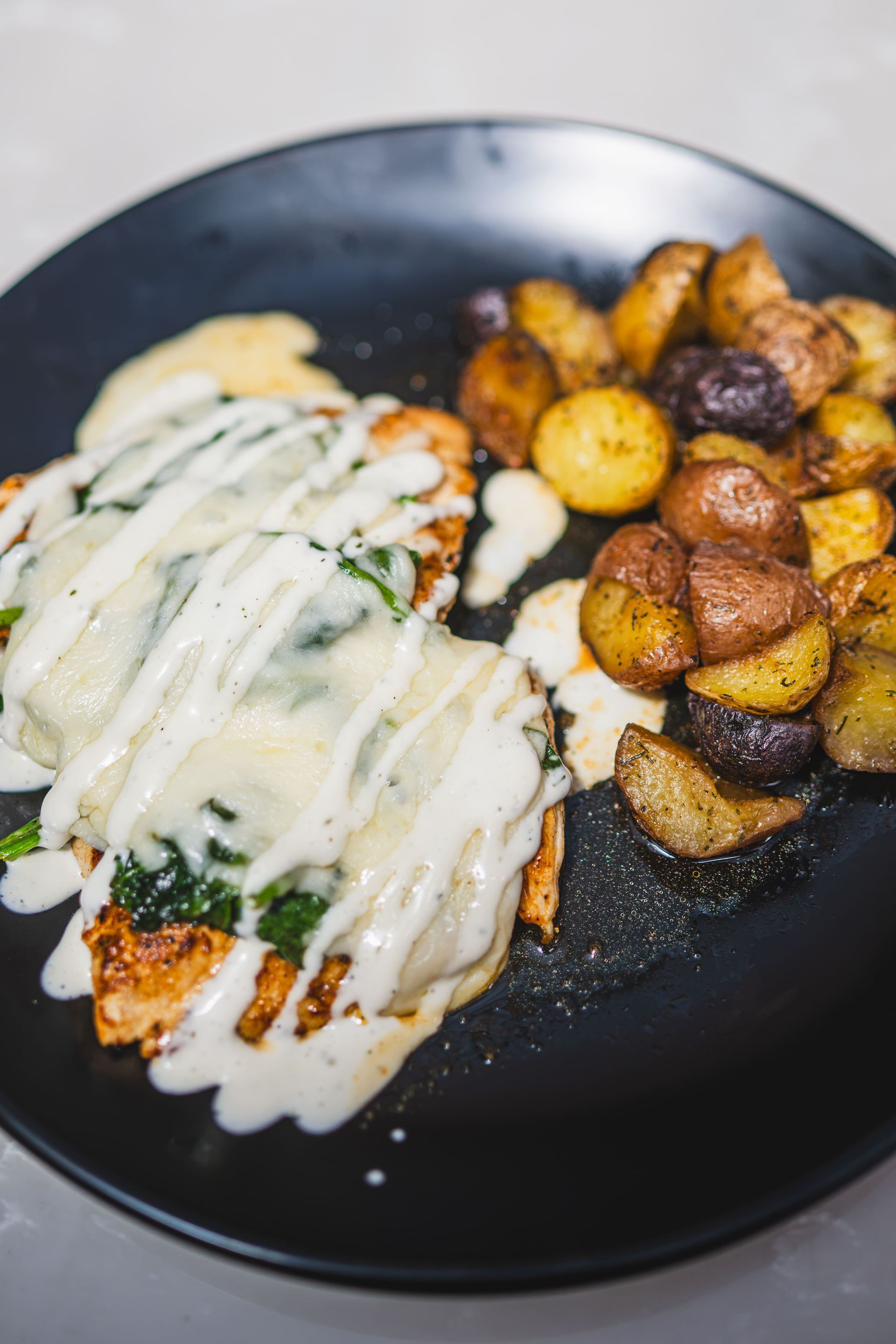 Black plate with melted cheese-covered entrée and roasted potatoes on the side