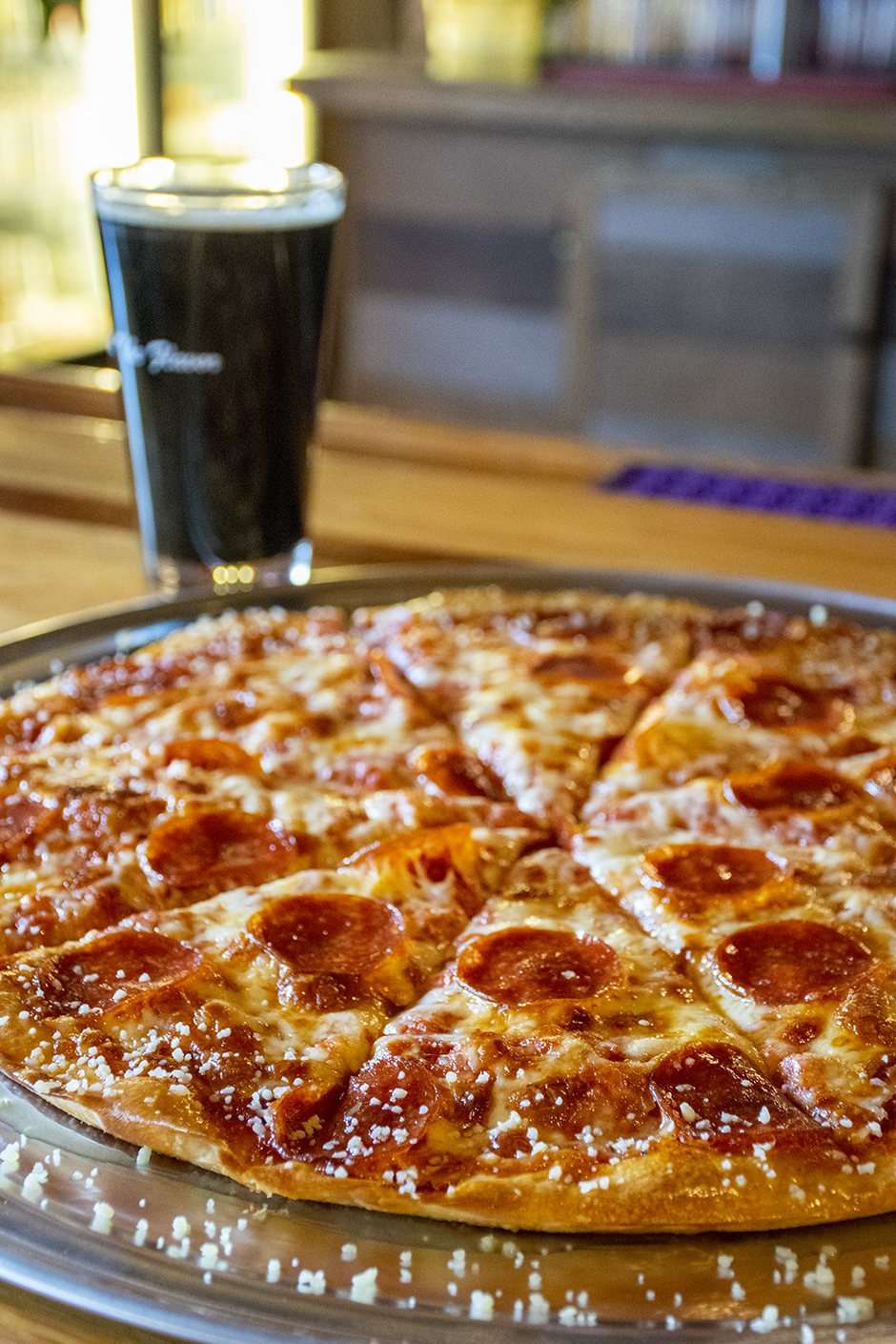 Pepperoni pizza on a table with a glass of dark soda in the background
