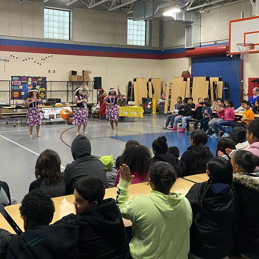 A group of people are sitting at tables in a gym watching a dance performance.