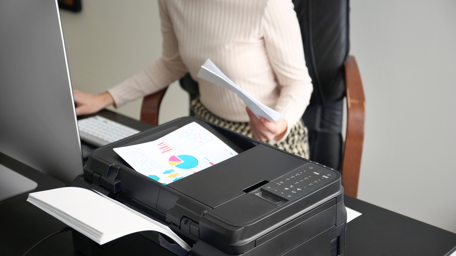 Person printing a document with a pie chart. Printer on a desk, near a computer.