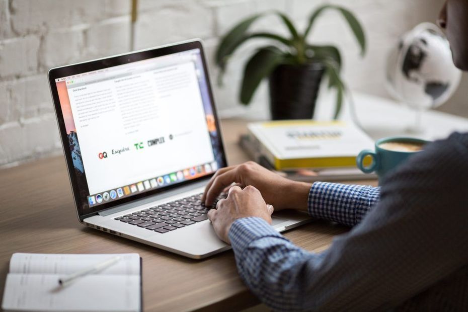 Person typing on laptop at desk with coffee cup, books, and globe in the background.