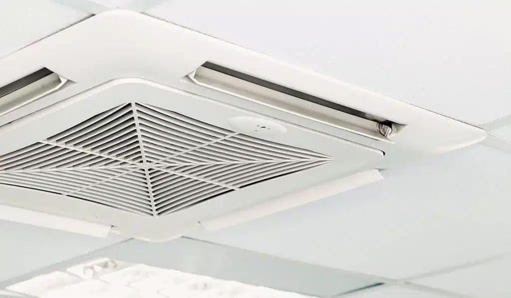 Several large outdoor air conditioning units lined up next to a stone wall and shrubs.