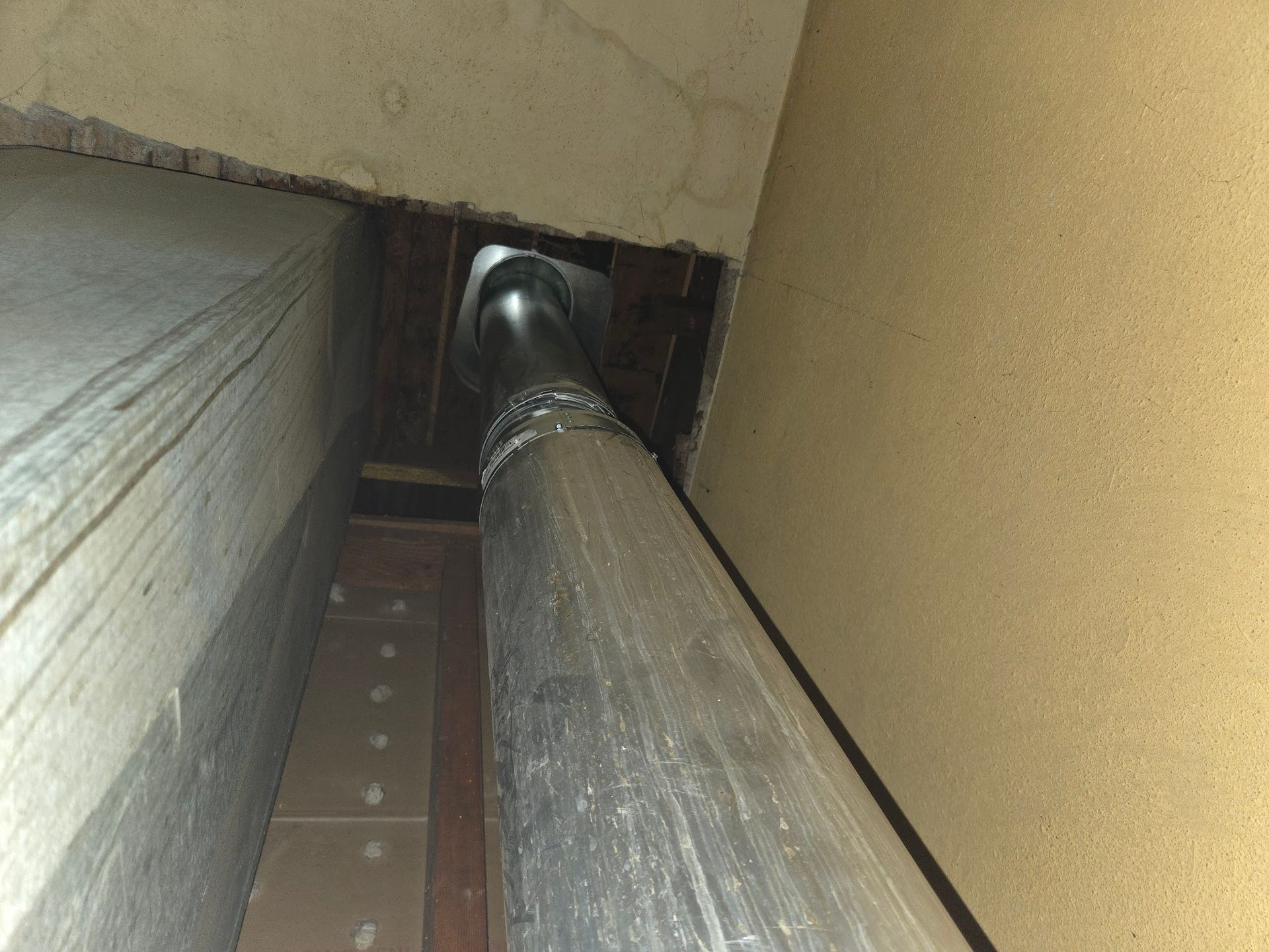 Metal ductwork running through a narrow space between walls, viewed from below.