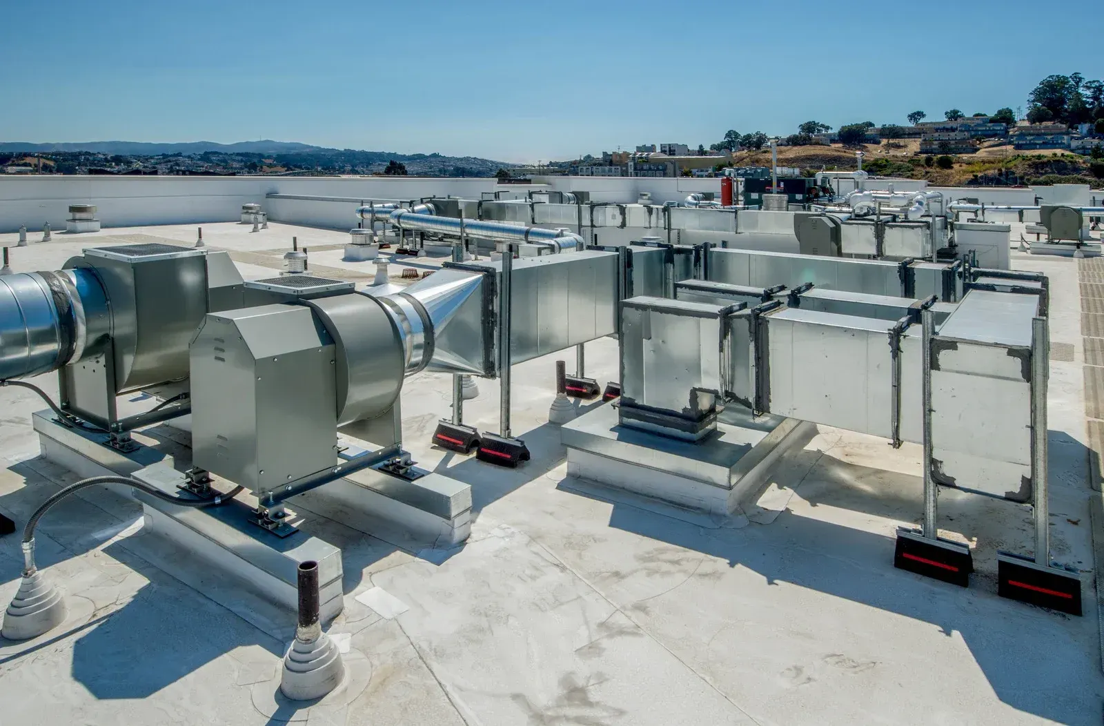 Rooftop HVAC system with metal ducts and vents on a white surface, sunny day.
