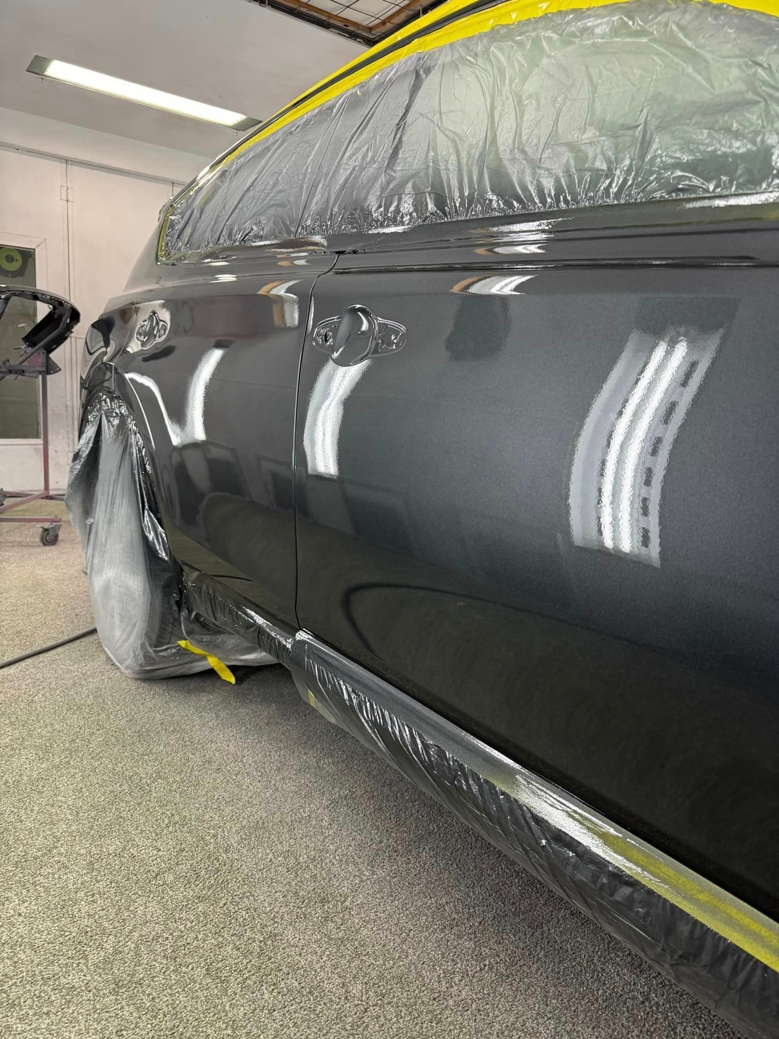 A black car is being painted in a garage.