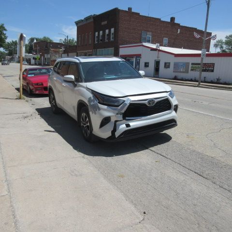 White Toyota SUV with front-end damage parked on a street in front of buildings. Red car visible on the left.