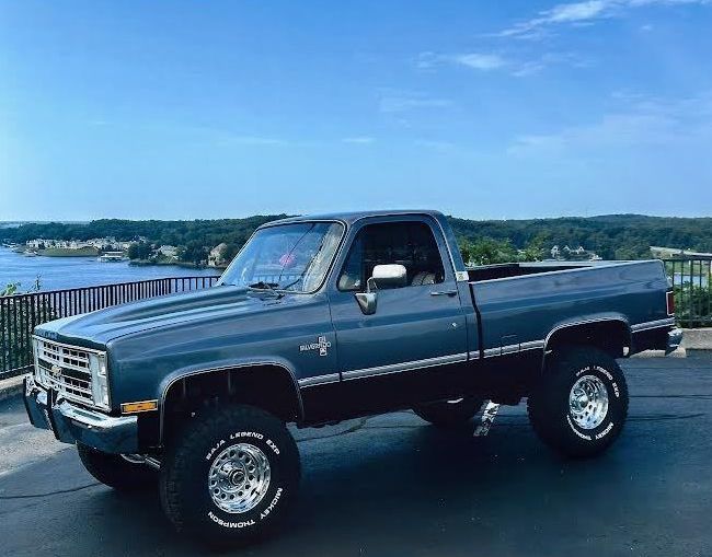 Blue lifted Chevrolet pickup truck with chrome accents, overlooking water.