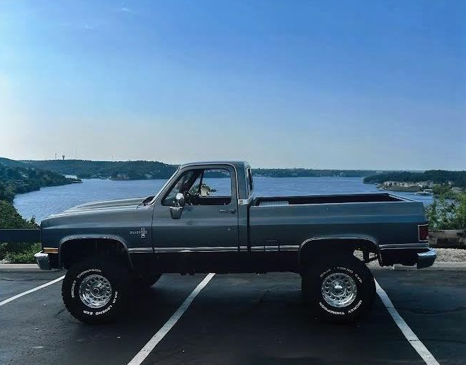 Gray lifted Chevy truck parked overlooking a lake and blue sky.