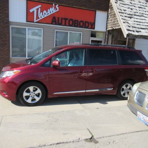 Maroon minivan parked outside Thom's Autobody shop in front of a building.