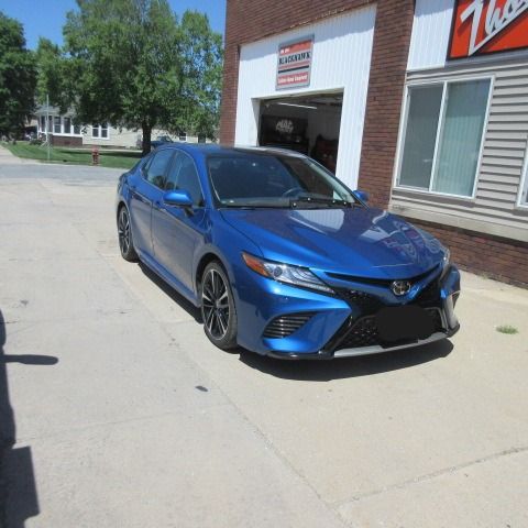 Gray Toyota Camry parked in front of a building with a window and wooden exterior.