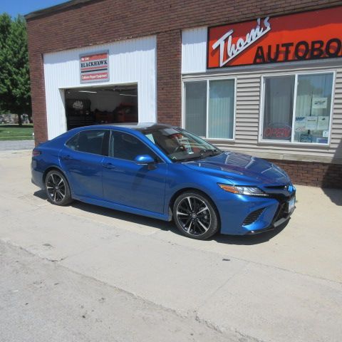 Gray sedan parked on sidewalk in front of an autobody shop.