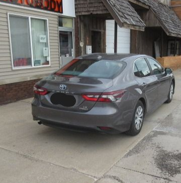Gray Toyota Camry parked in front of a building with a window and wooden exterior.