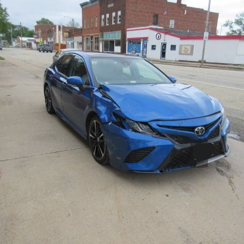 Damaged gray sedan with an open trunk and dented rear. Street scene.