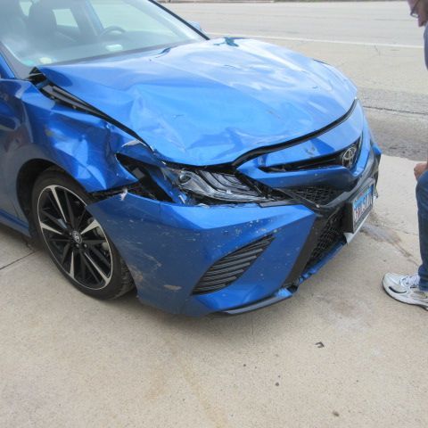 A gray car with a dent in the rear panel, near the taillight and tire.