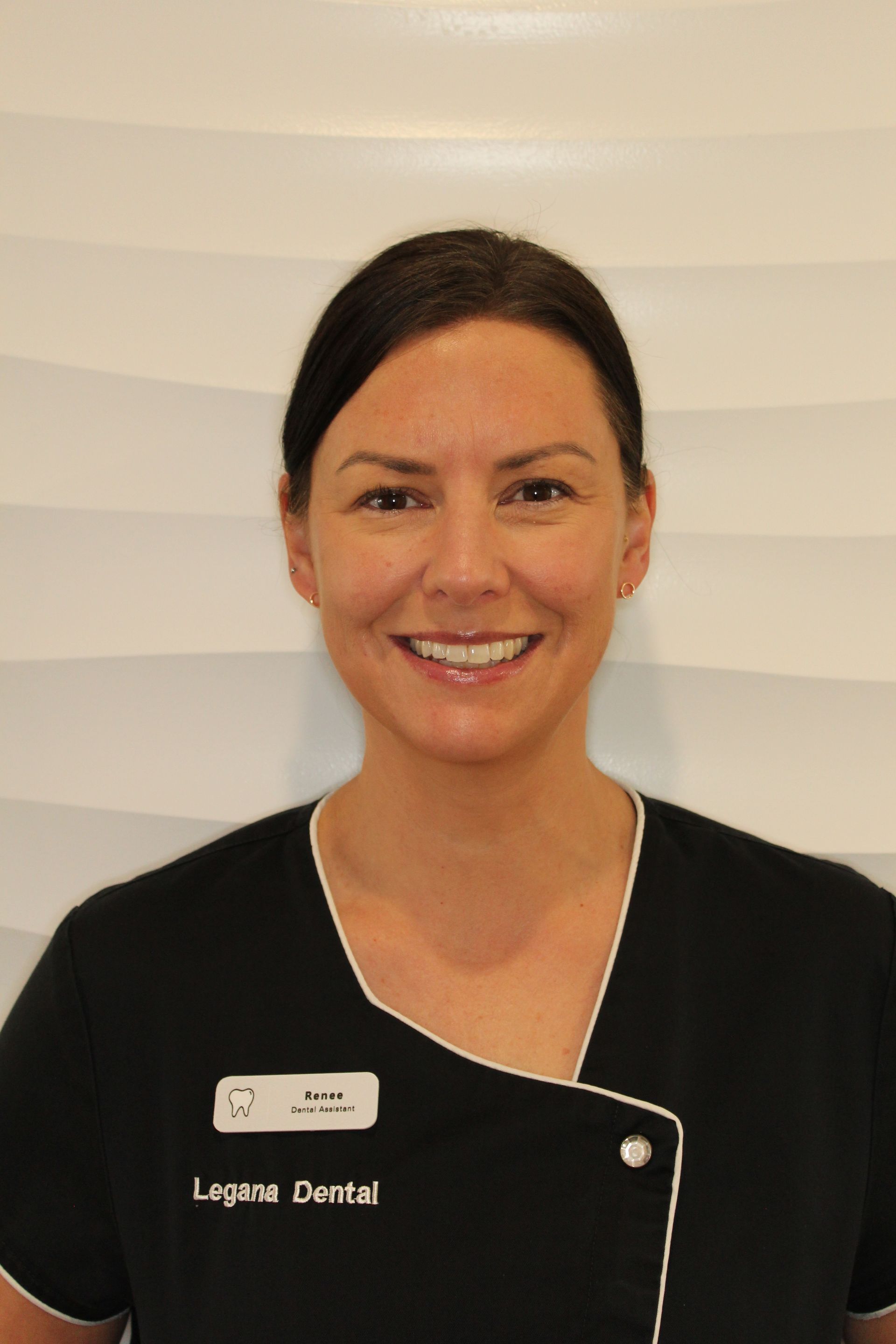Smiling dental staff member in black uniform against a light striped background