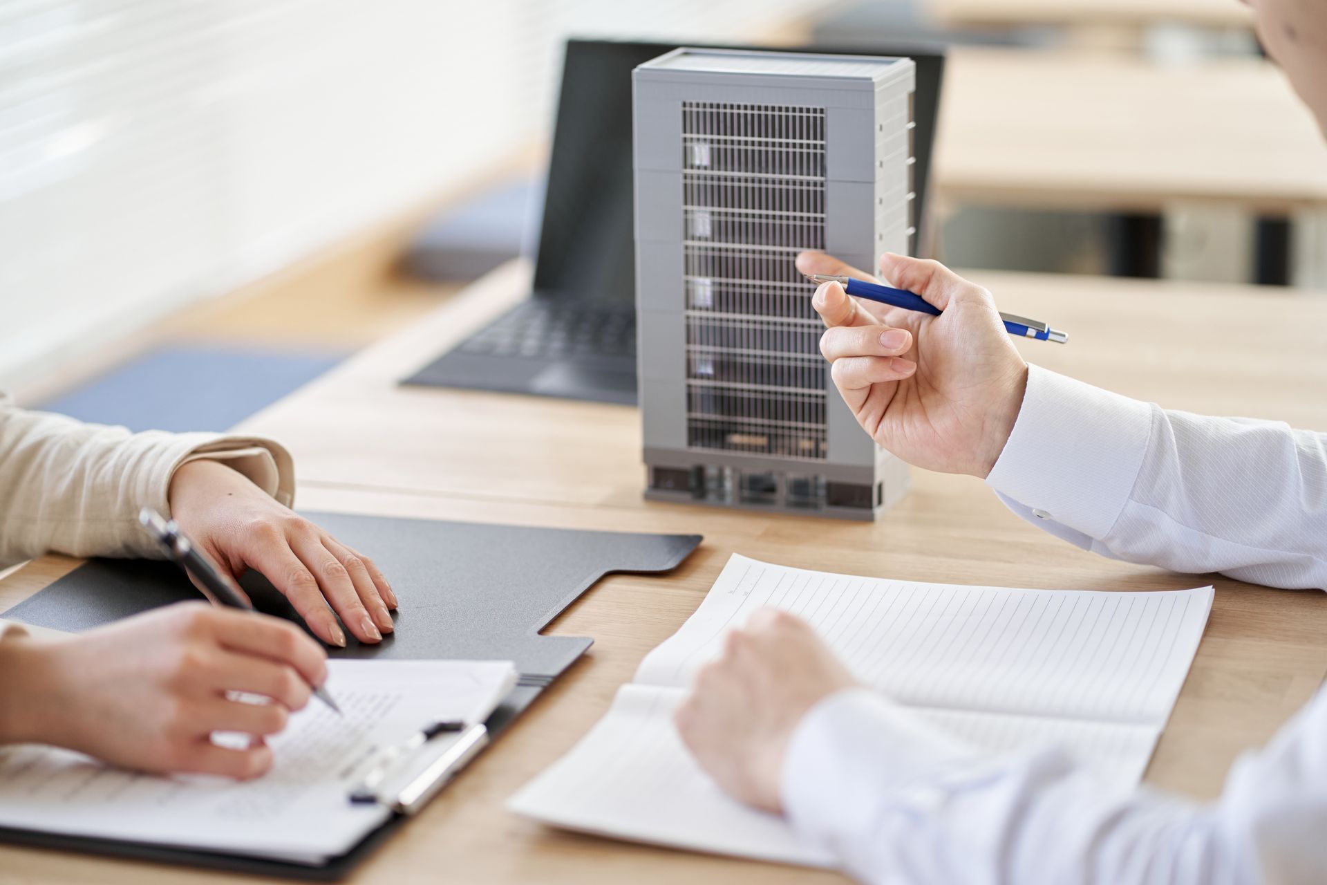 Hands reviewing charts and notes around a desk with a laptop and tablet, discussing a document