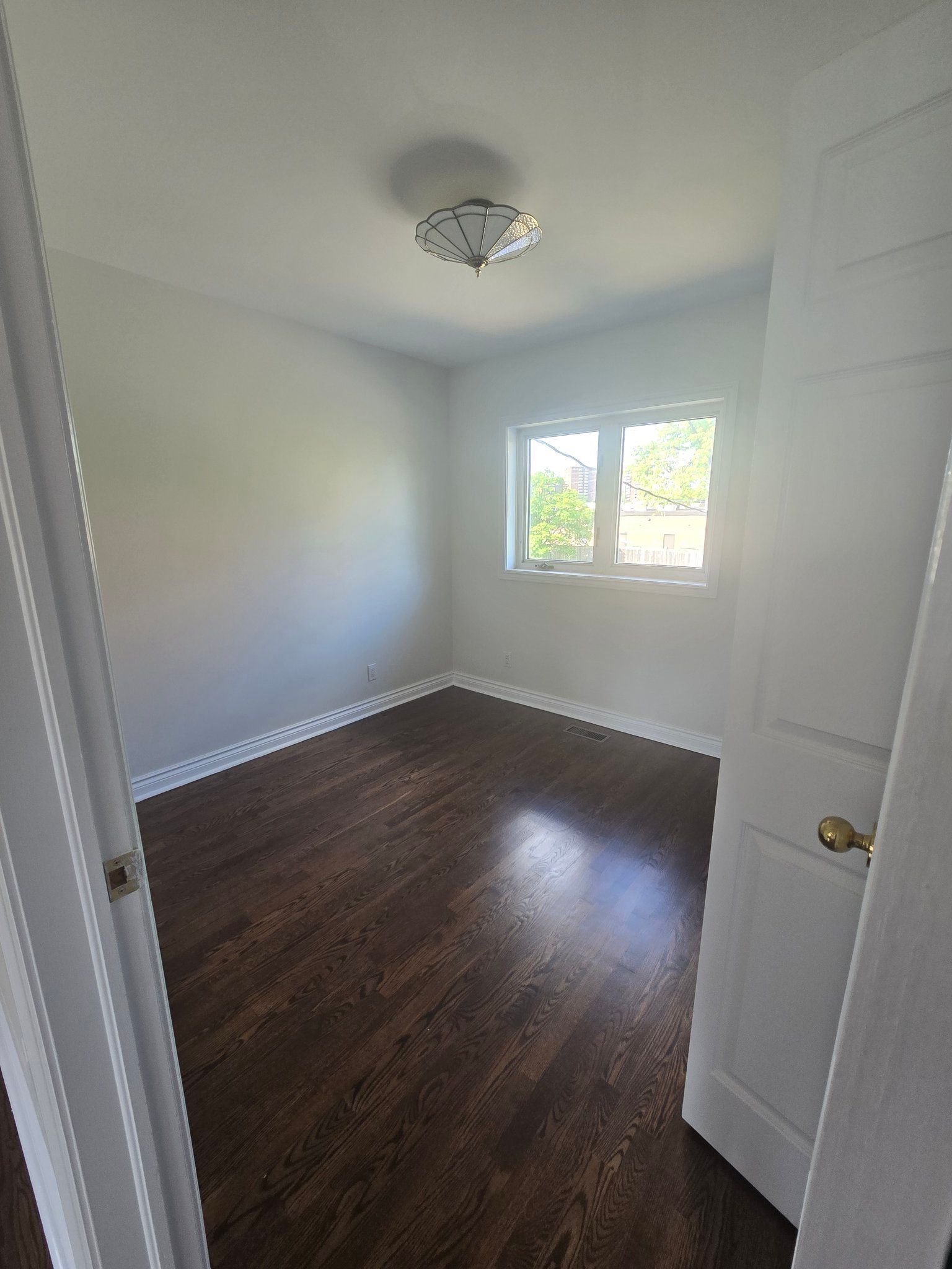 An empty bedroom with hardwood floors and white walls.