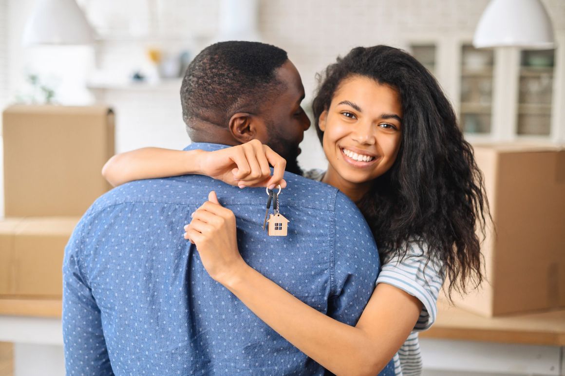 A woman is holding a pair of keys behind a man 's back.