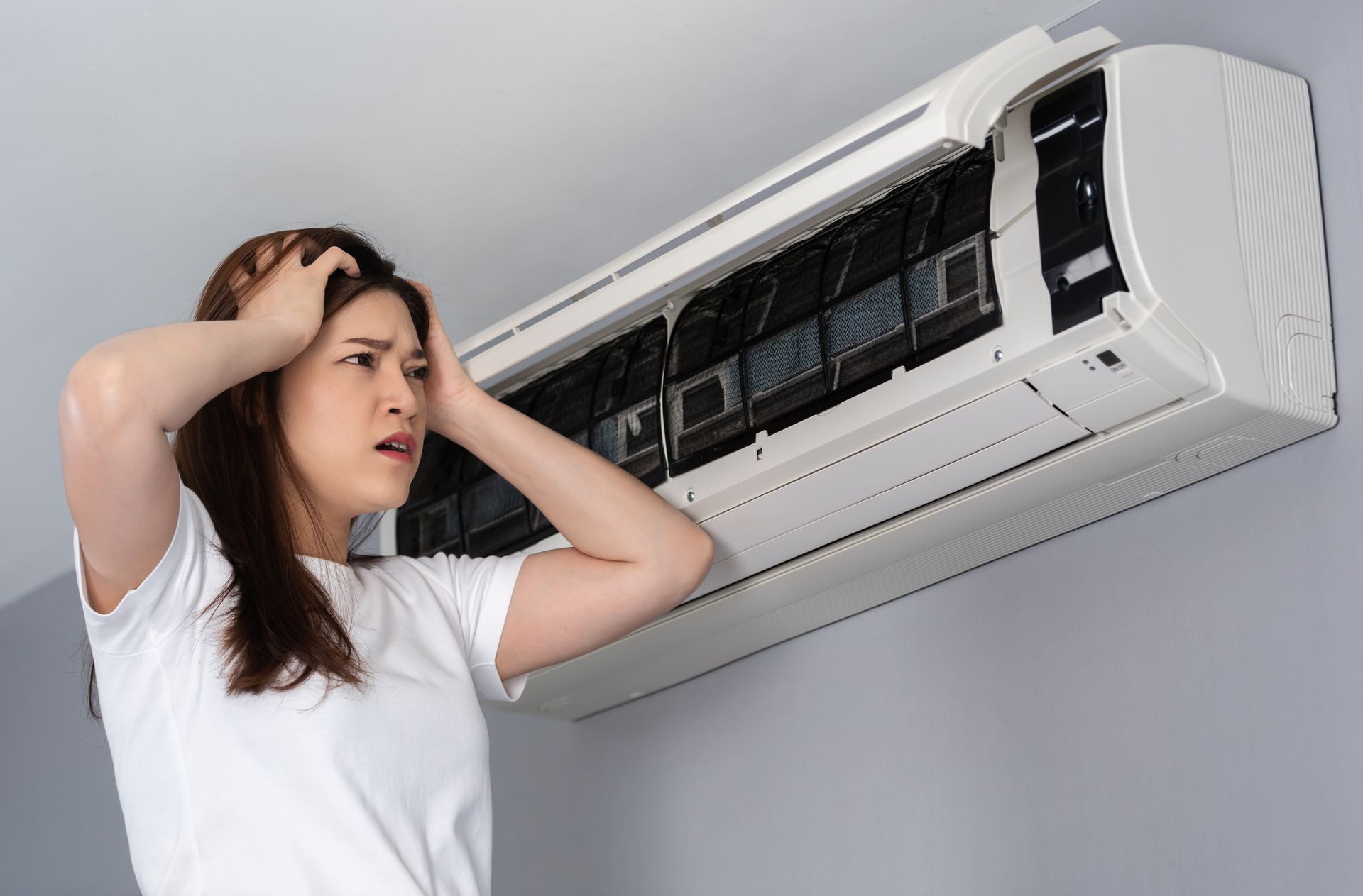 Une femme se tient devant un climatiseur cassé.