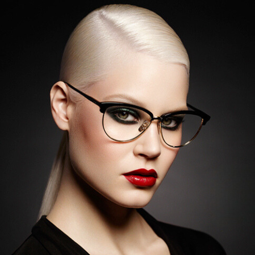 Woman with platinum blonde hair, wearing glasses, dark eye makeup, and red lipstick.