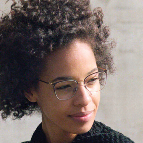 Woman with curly hair wearing glasses, looking to the side with a slight smile.