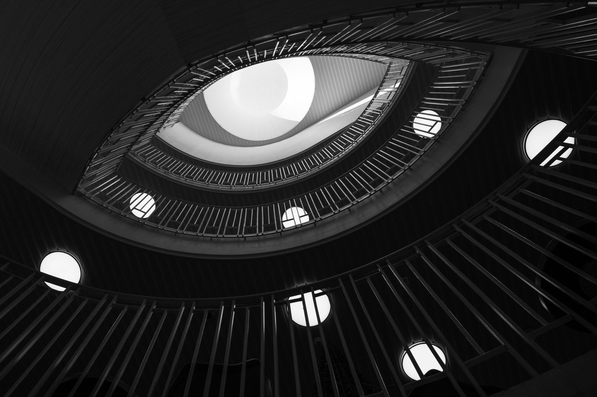 A spiral staircase viewed from below, with circular windows and natural light at the top.