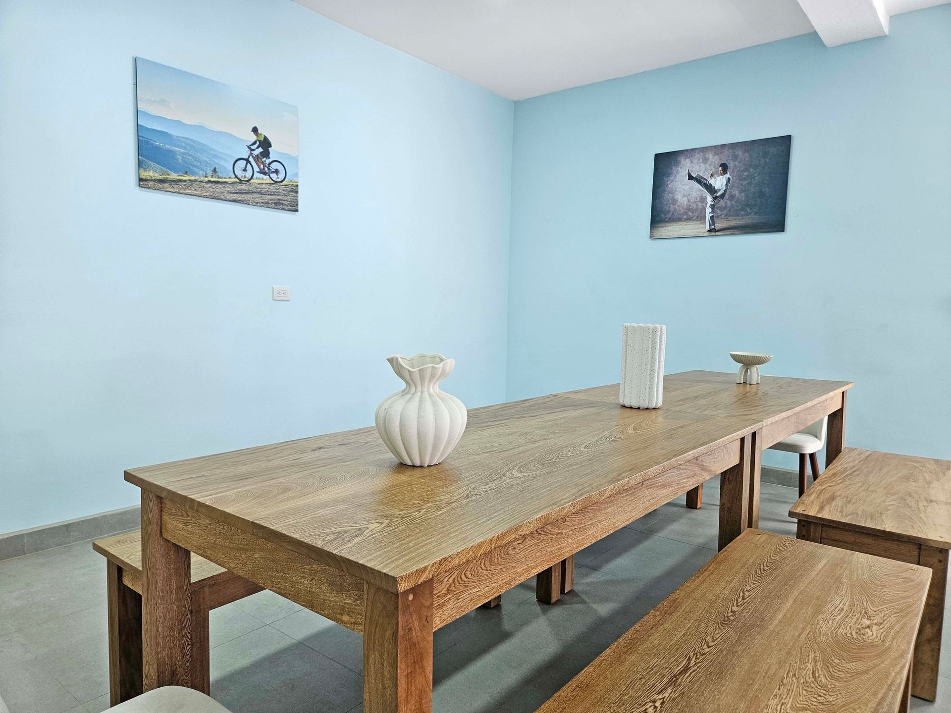 A dining room with a long wooden table, benches, and art on light blue walls.