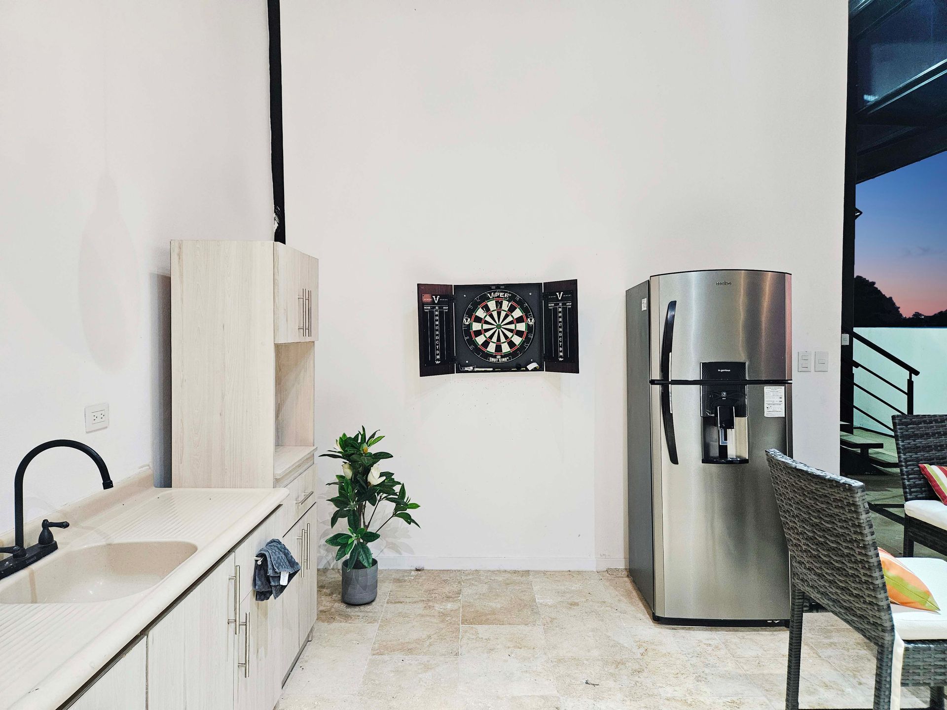 Outdoor kitchen with cabinets, sink, fridge, dartboard, and patio furniture.