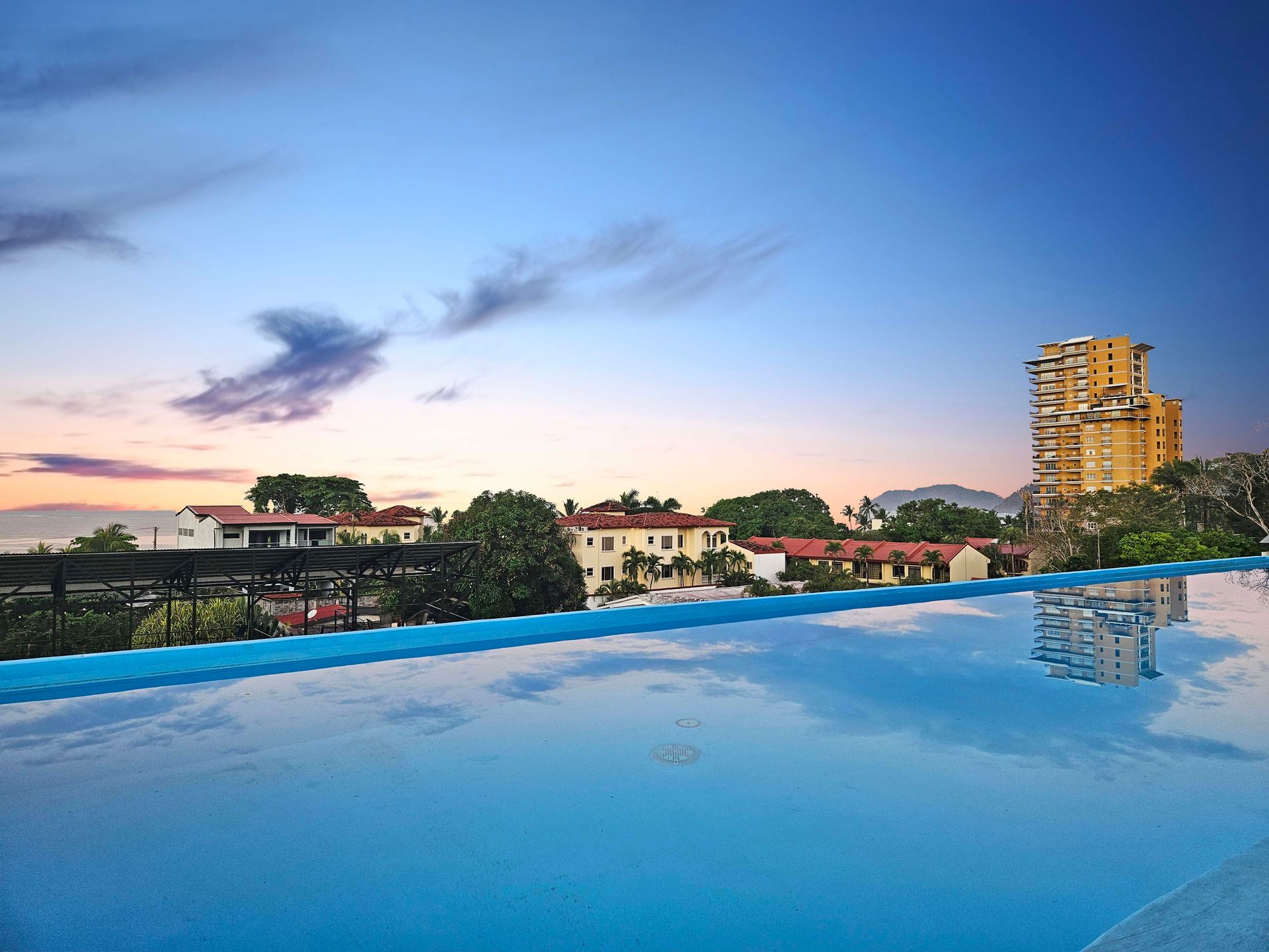 Infinity pool overlooking a city with blue sky at dusk.