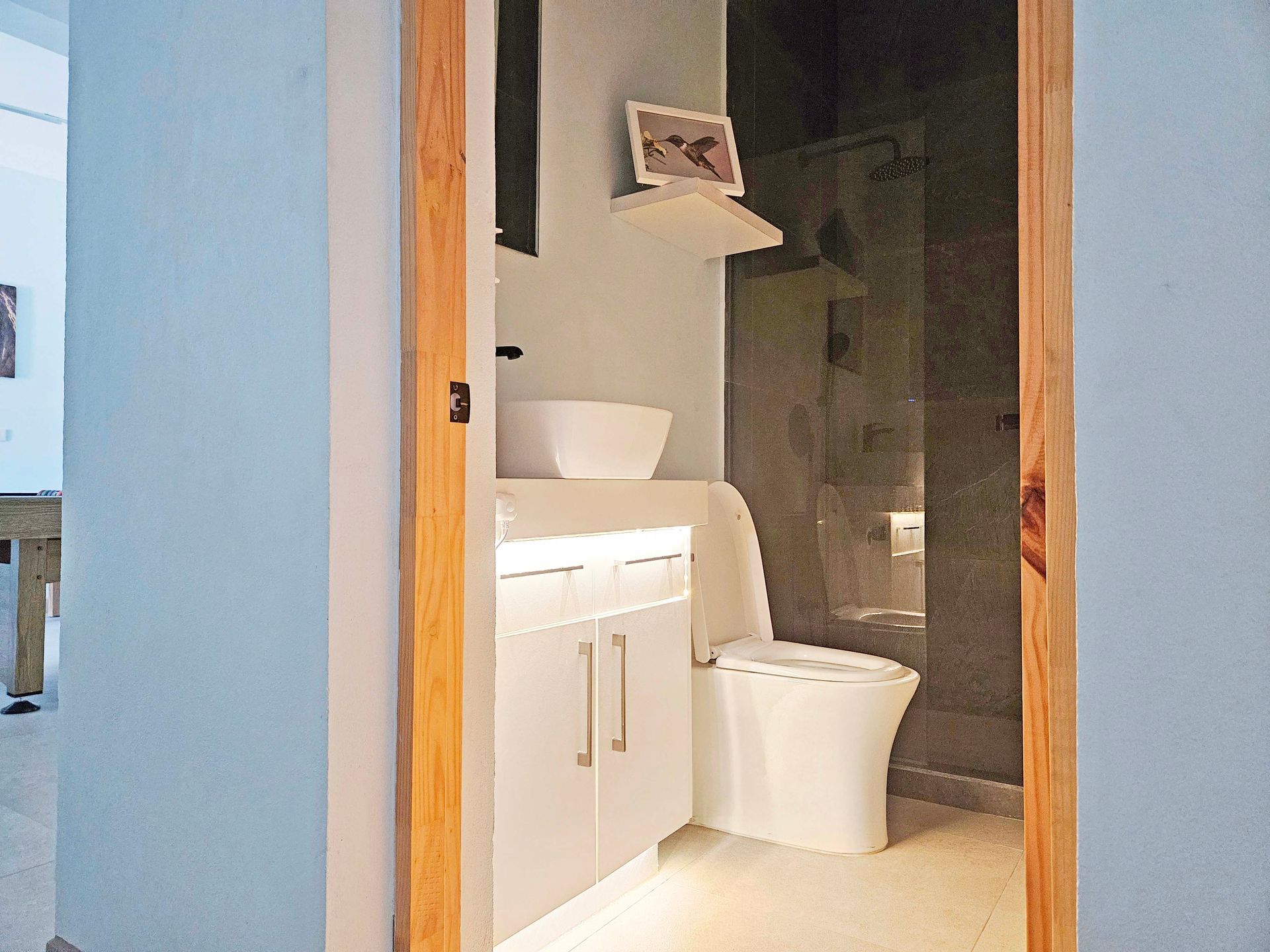 Bathroom interior through doorway: white toilet, sink, and vanity with wooden door frame.