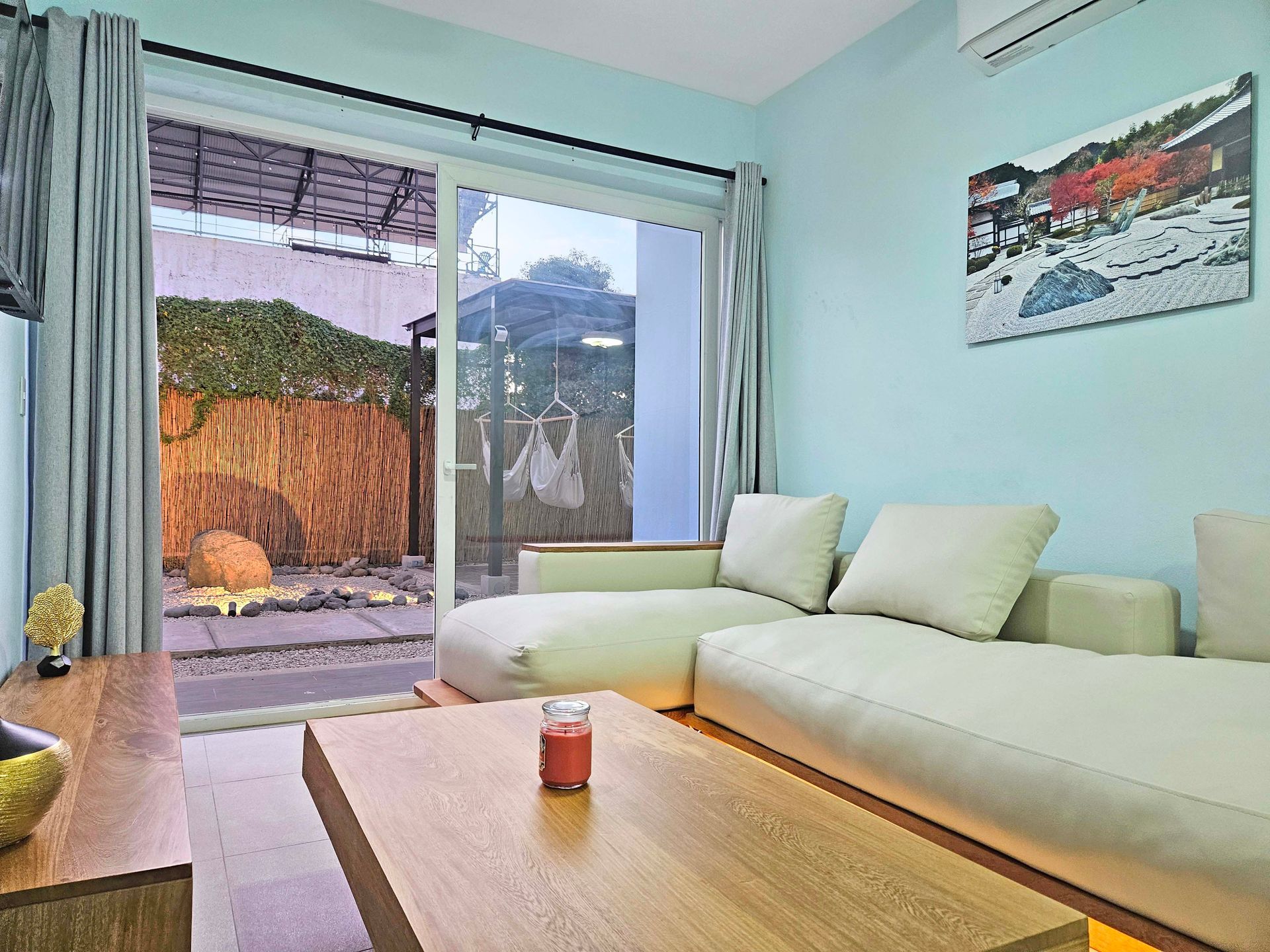 A living room with a light blue wall and a white couch. A sliding glass door leads to a garden.