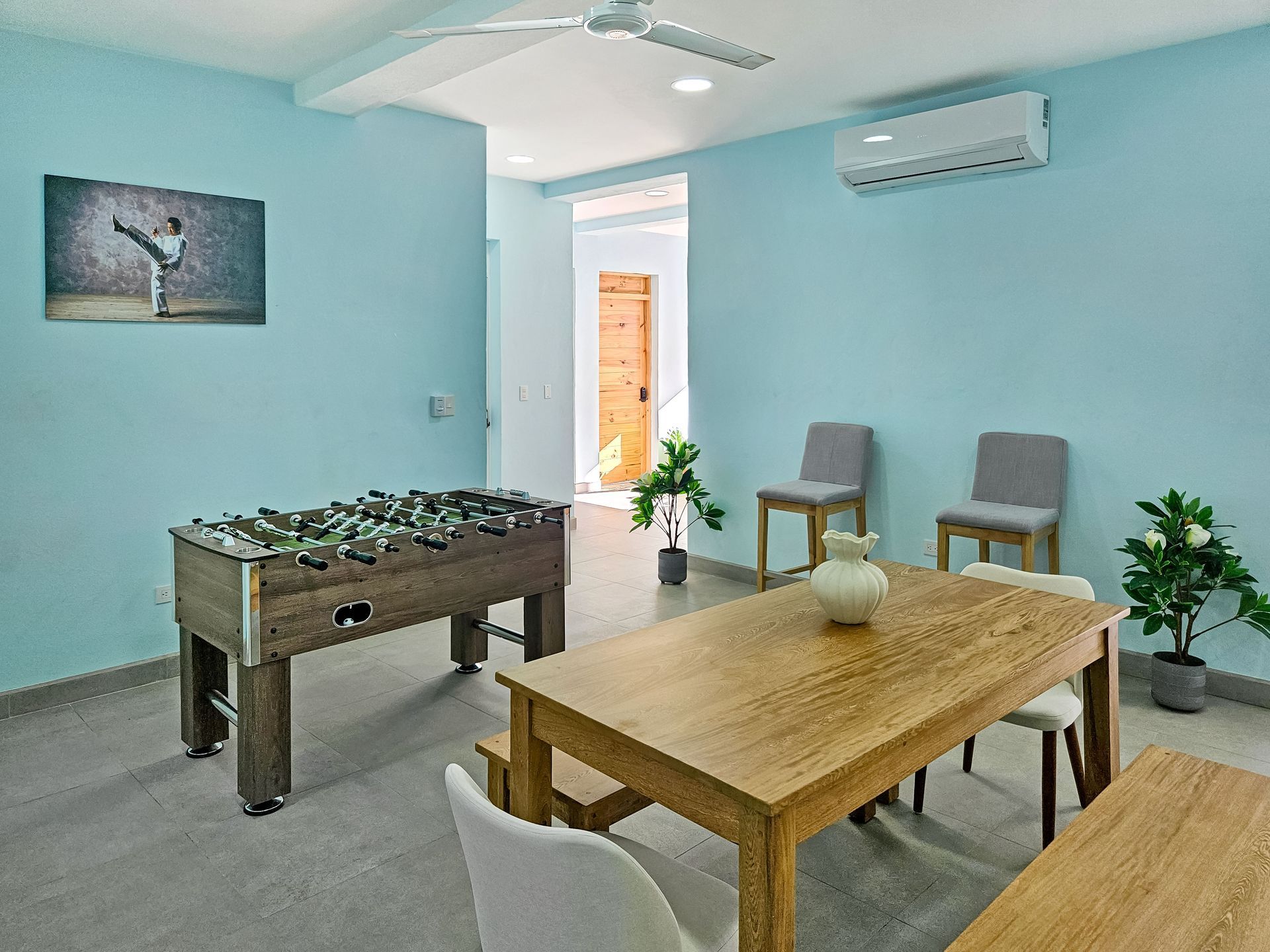 A room with a foosball table, dining table, chairs, and light blue walls.