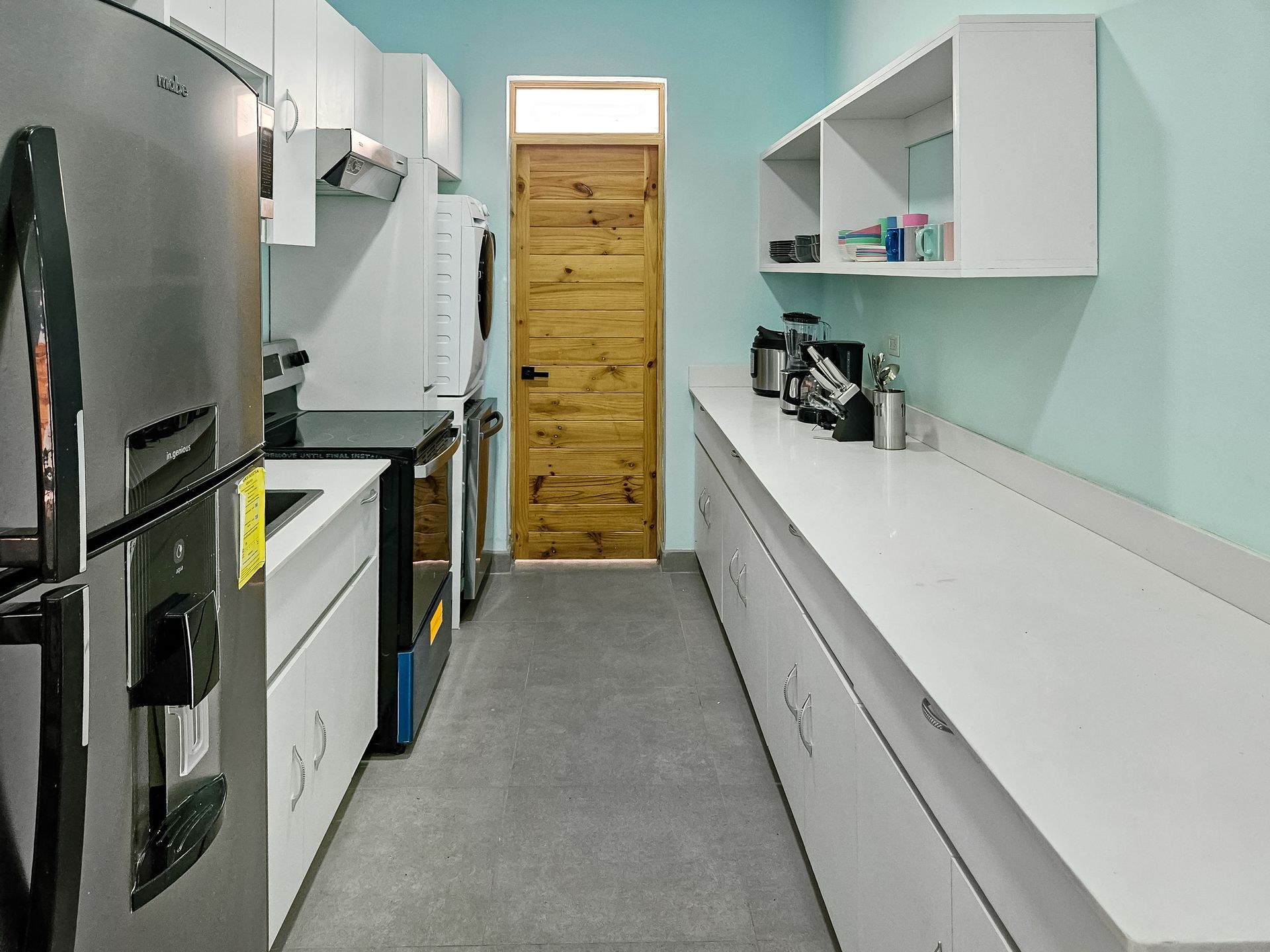 Narrow kitchen with white cabinets, stainless steel appliances, light blue walls, and a wooden door.