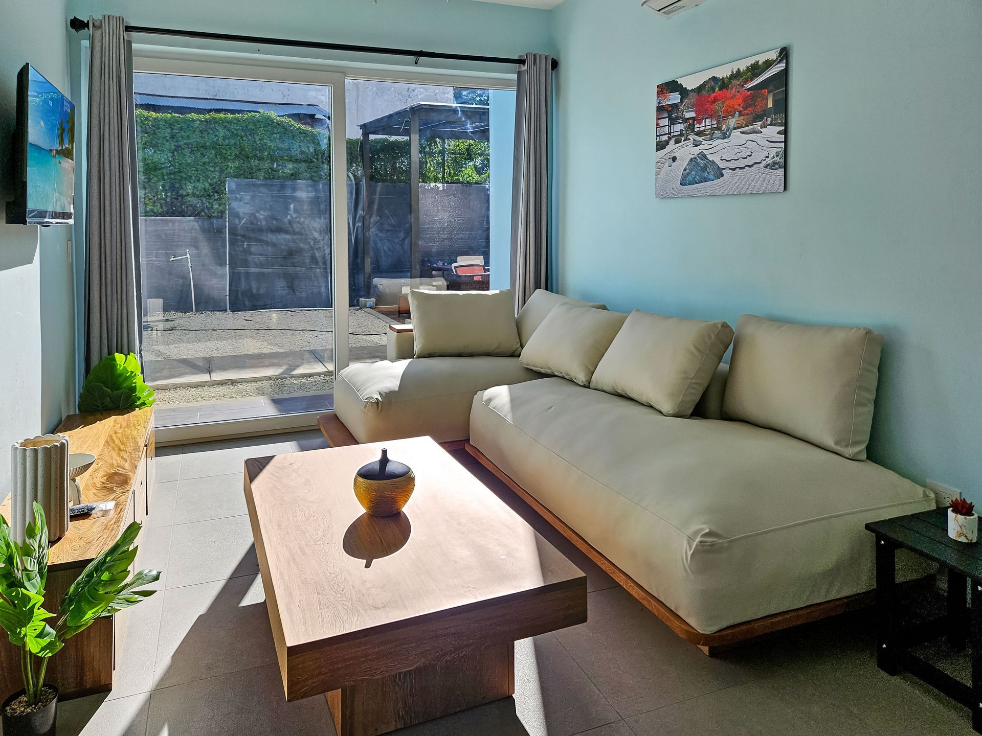 Living room with light blue walls, beige sectional sofa, sliding glass door, and a wooden coffee table.
