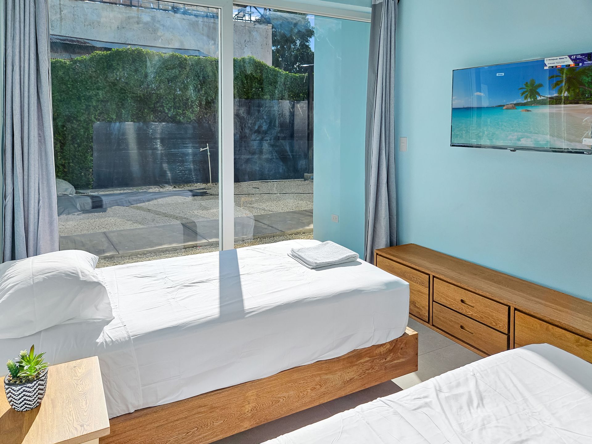 Bedroom with two twin beds, large window, turquoise walls, and beach scene art.