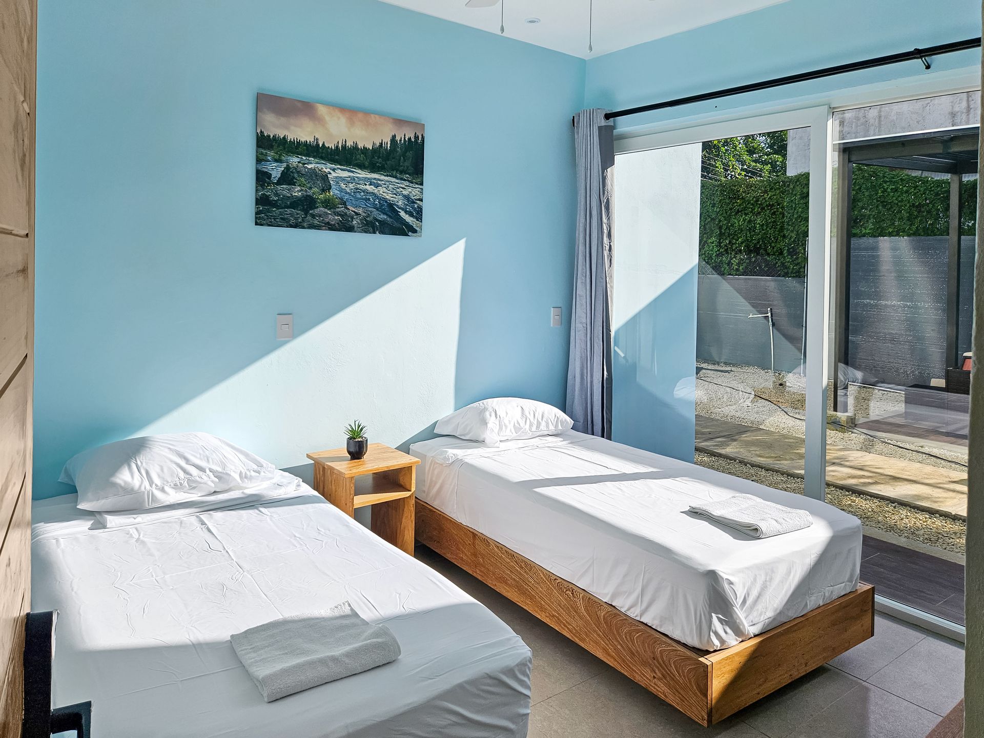Two twin beds in a room with blue walls, sliding glass door, and landscape art.
