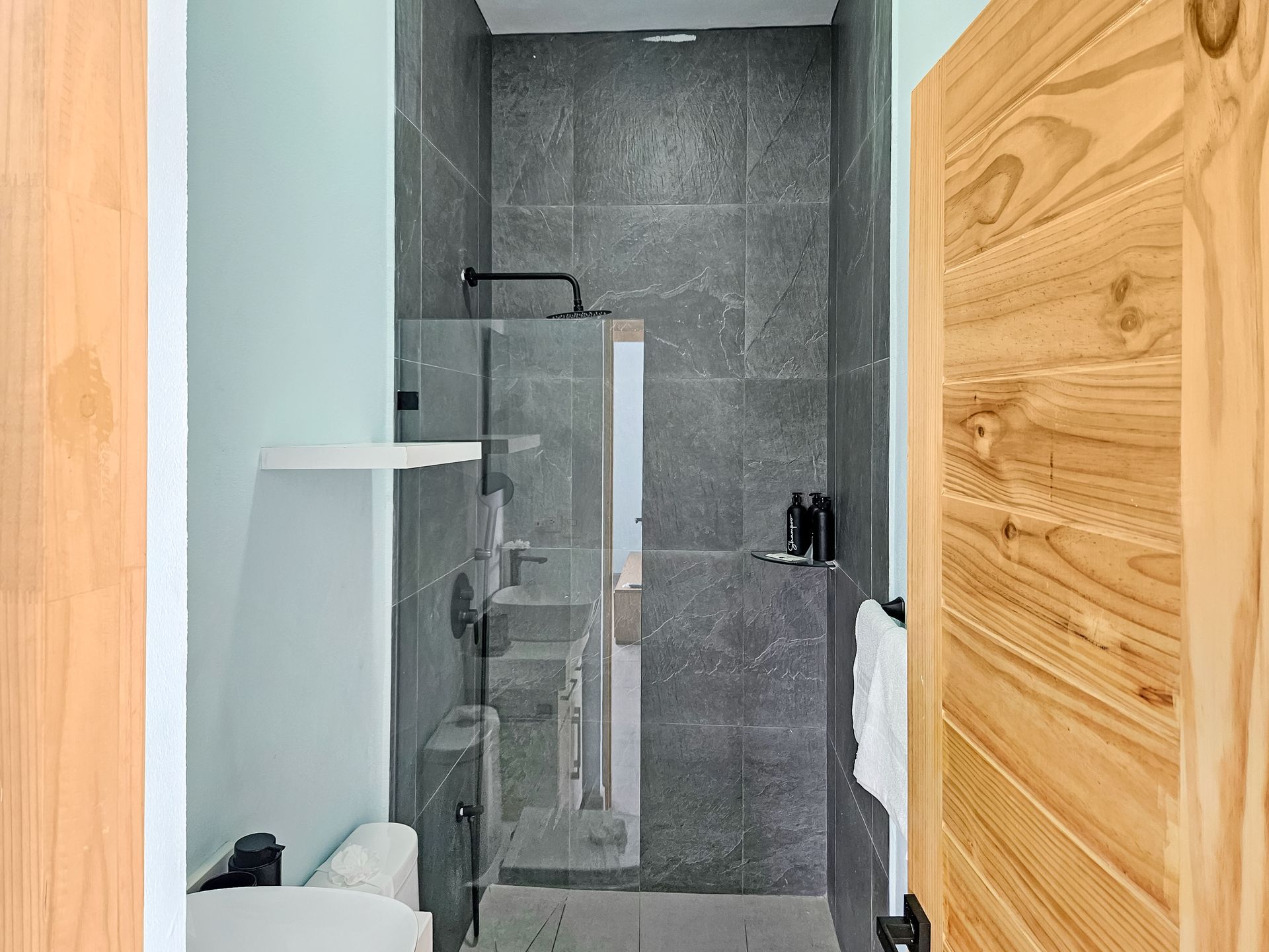 Small modern bathroom with gray tile shower and wooden door.