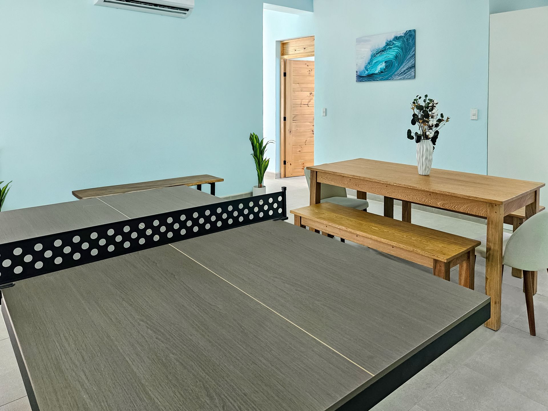 Ping pong table in a room with a dining table, light blue walls, and a wooden door.
