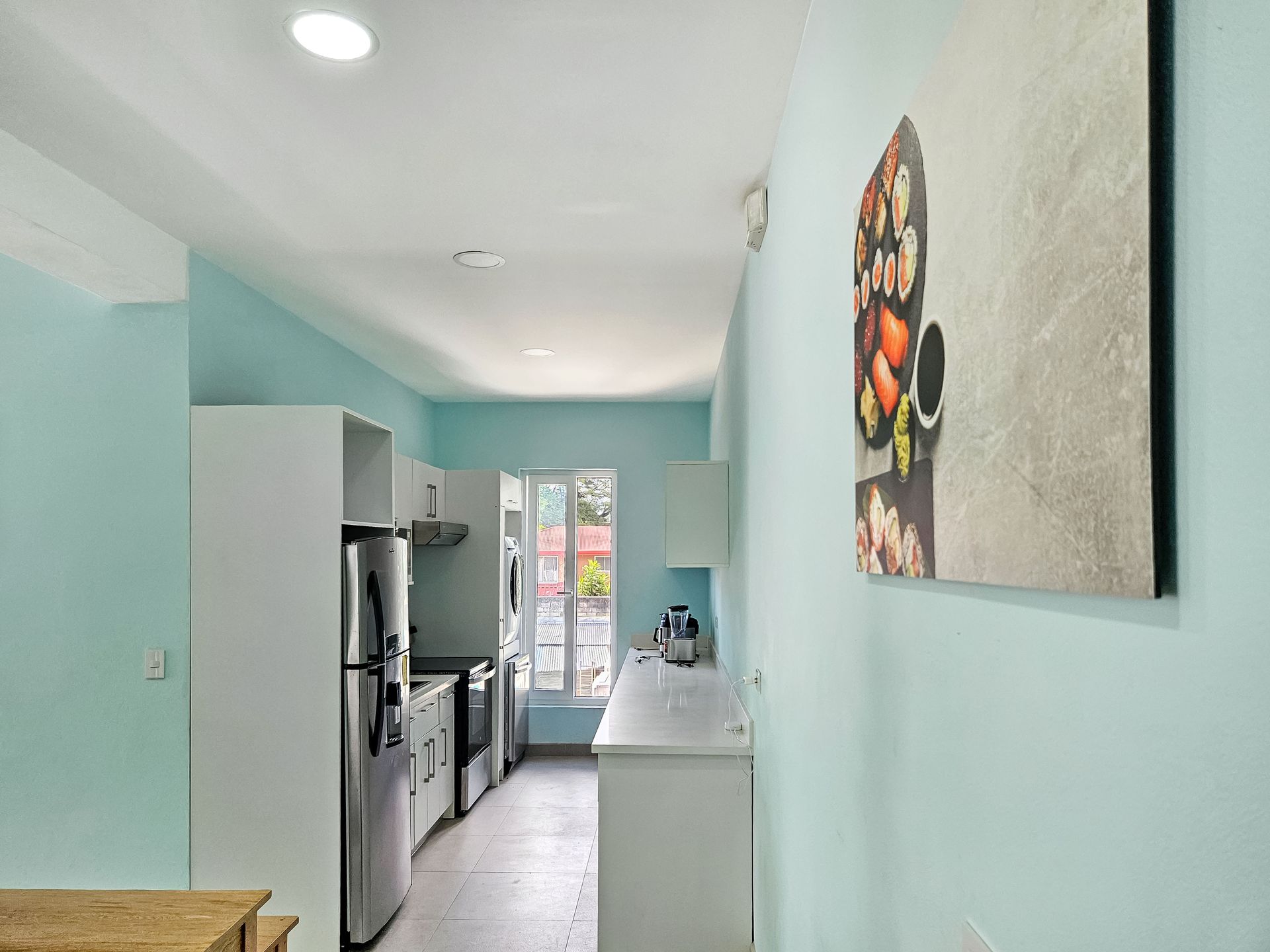 A narrow kitchen with white cabinets, stainless steel appliances, and turquoise walls.