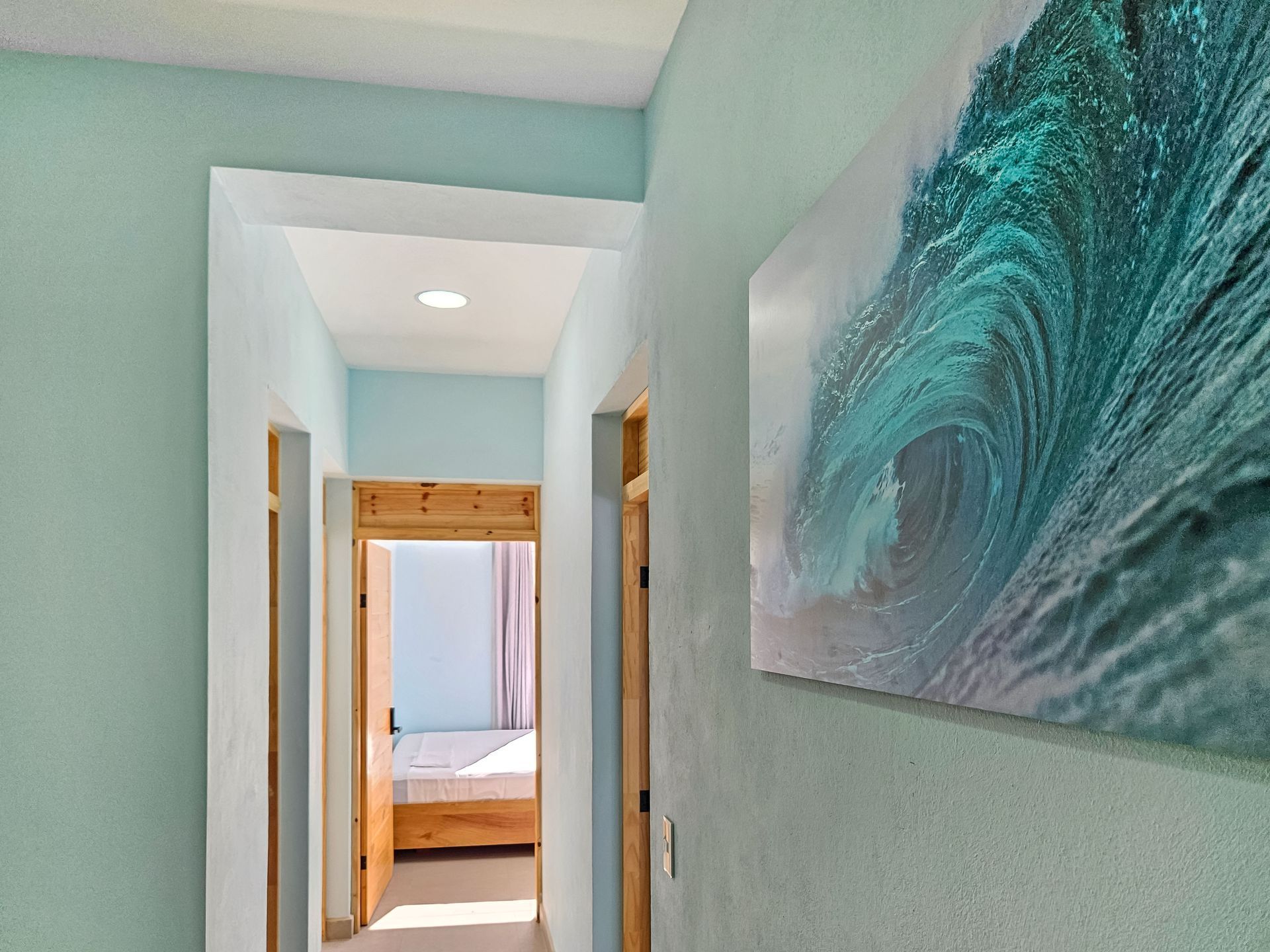 Long hallway painted light blue with wave art, leading to a bedroom with a bed.