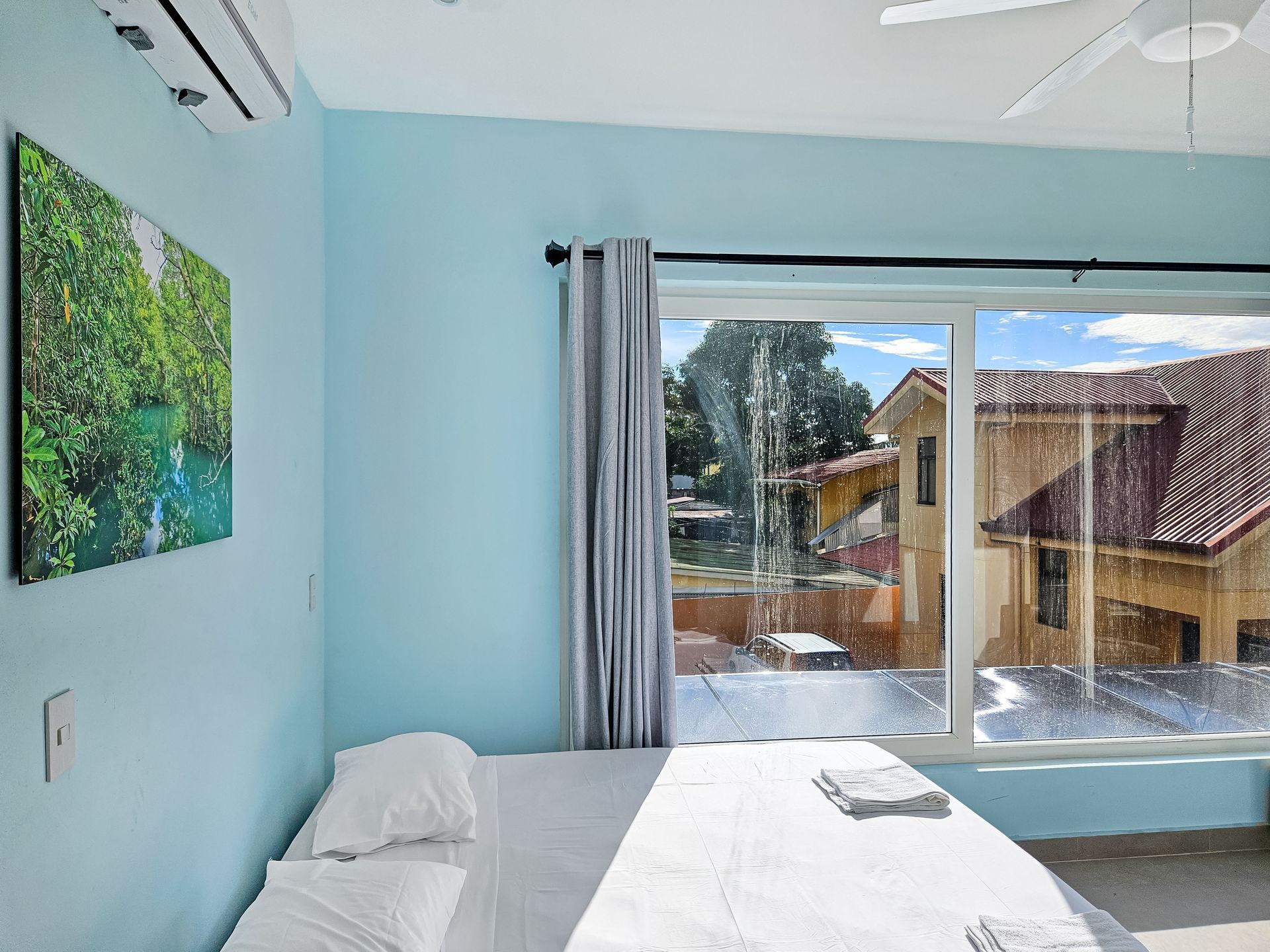 Bedroom with light blue walls, a bed, a window with a view, and artwork.