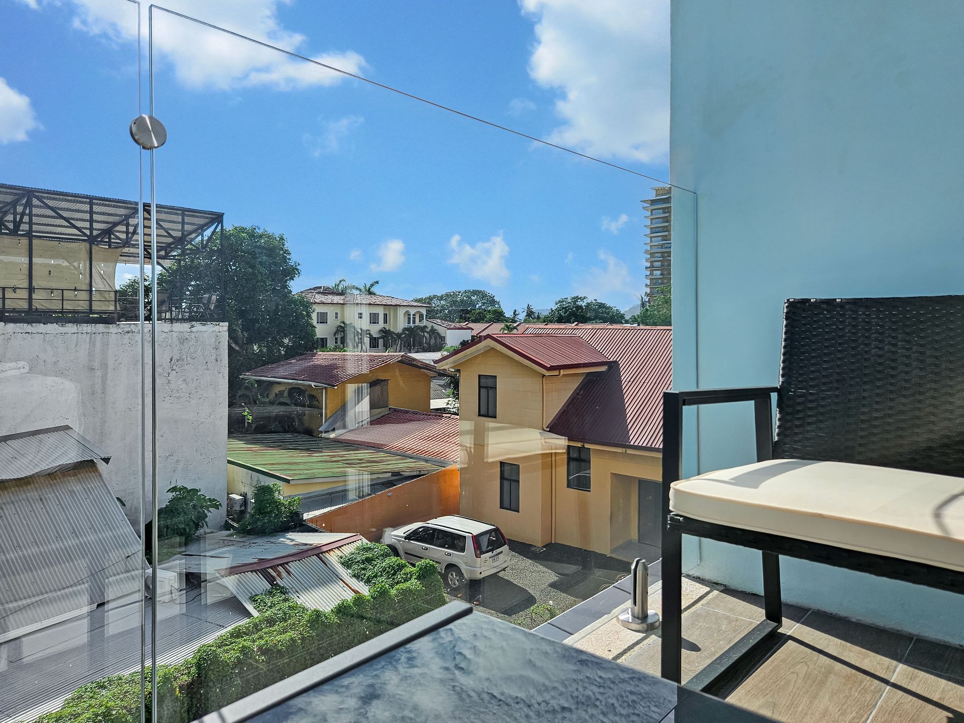 View from balcony with homes, blue sky. Chair on right.