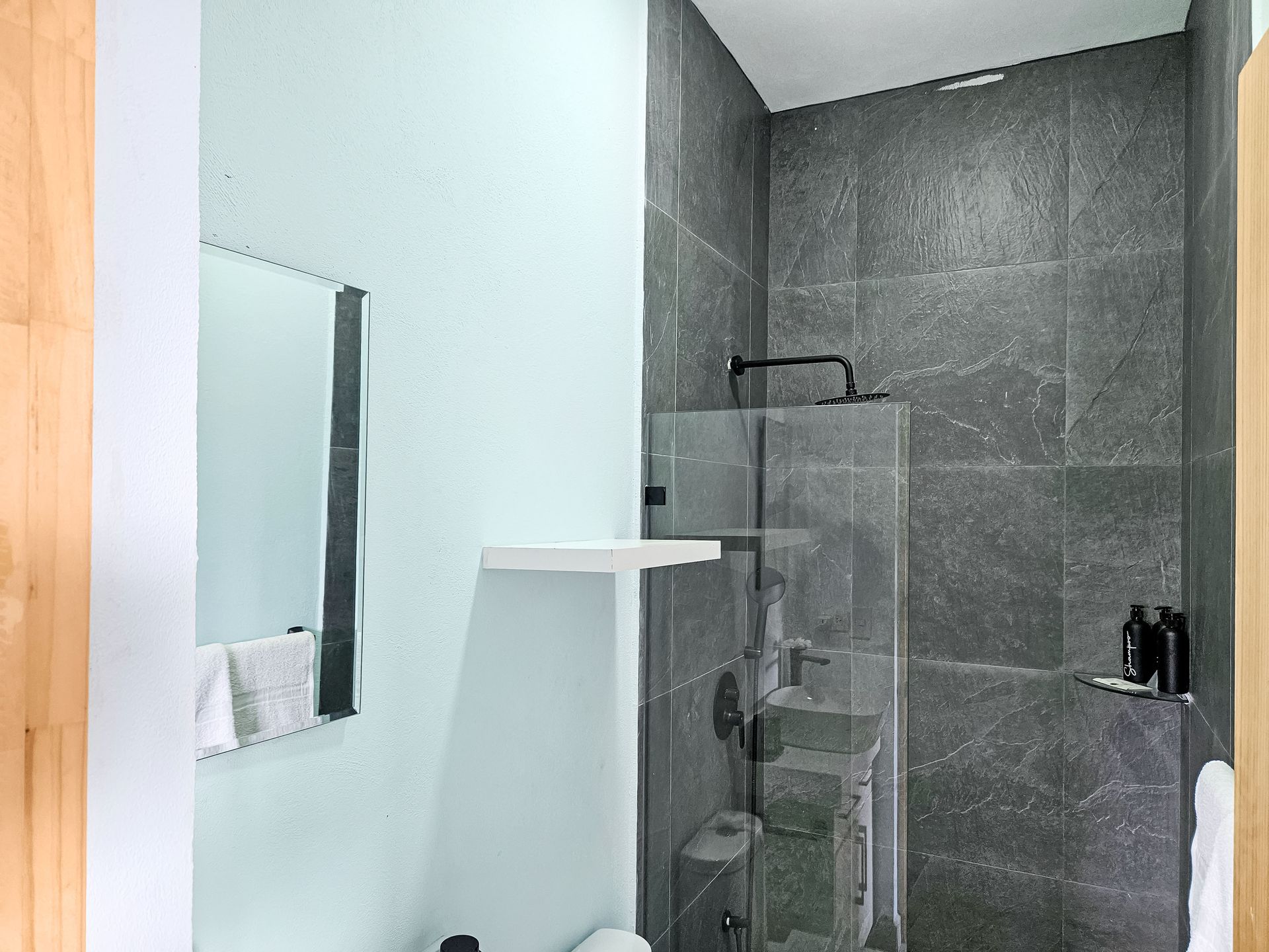 Bathroom with gray tiled shower, glass door, mirror, and pale blue wall.