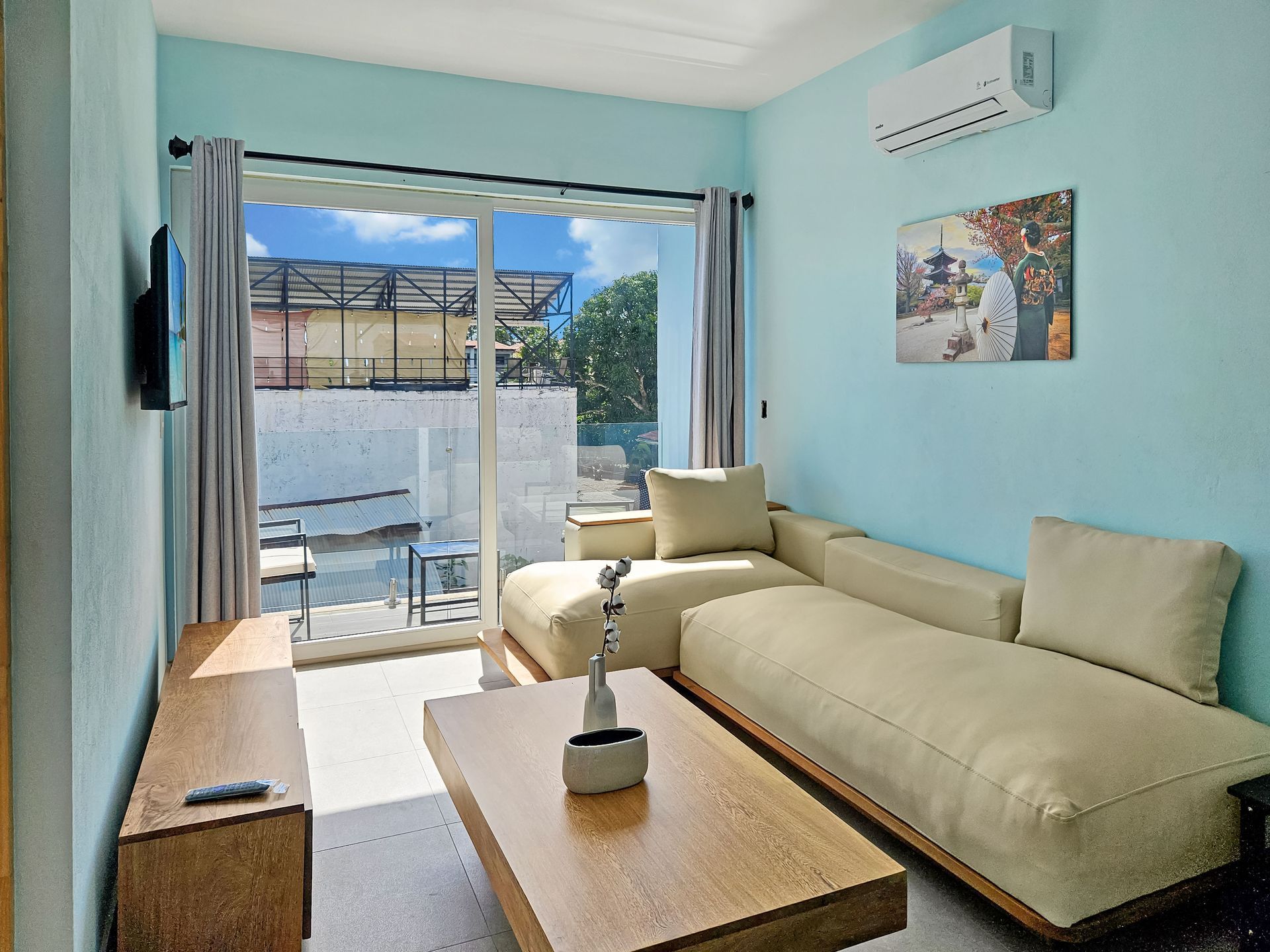 Living room with light blue walls, beige sectional sofa, and sliding door to balcony.