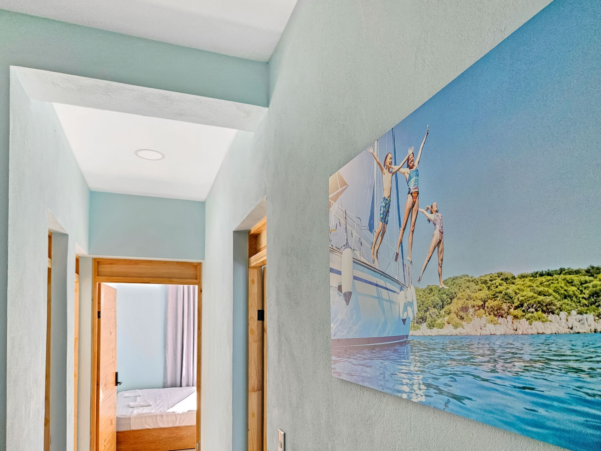 Hallway with a print of people diving off a boat into blue water. Light blue walls and wooden doors.