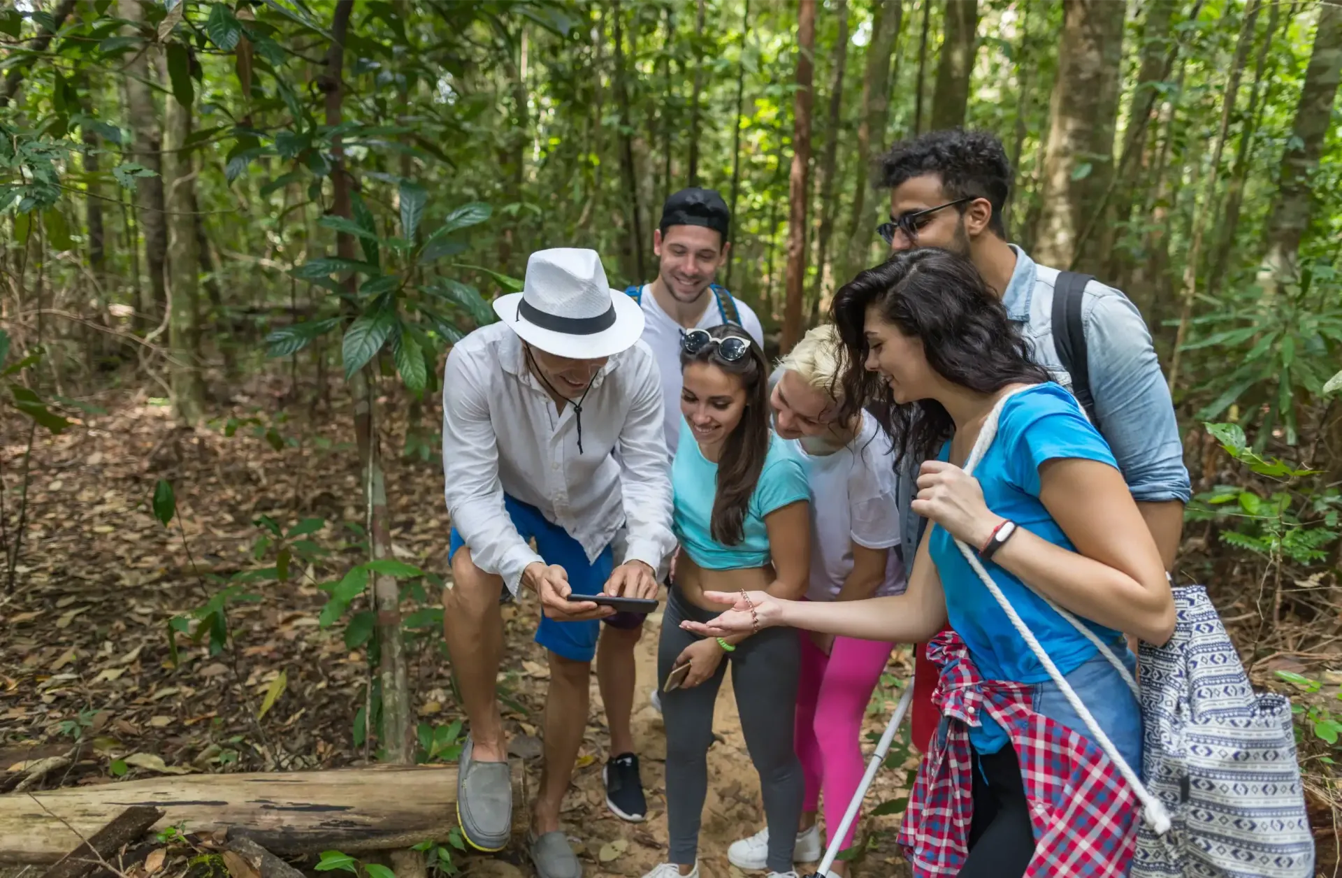 Group of people looking at a phone in a forest, the woman points at something on the ground.