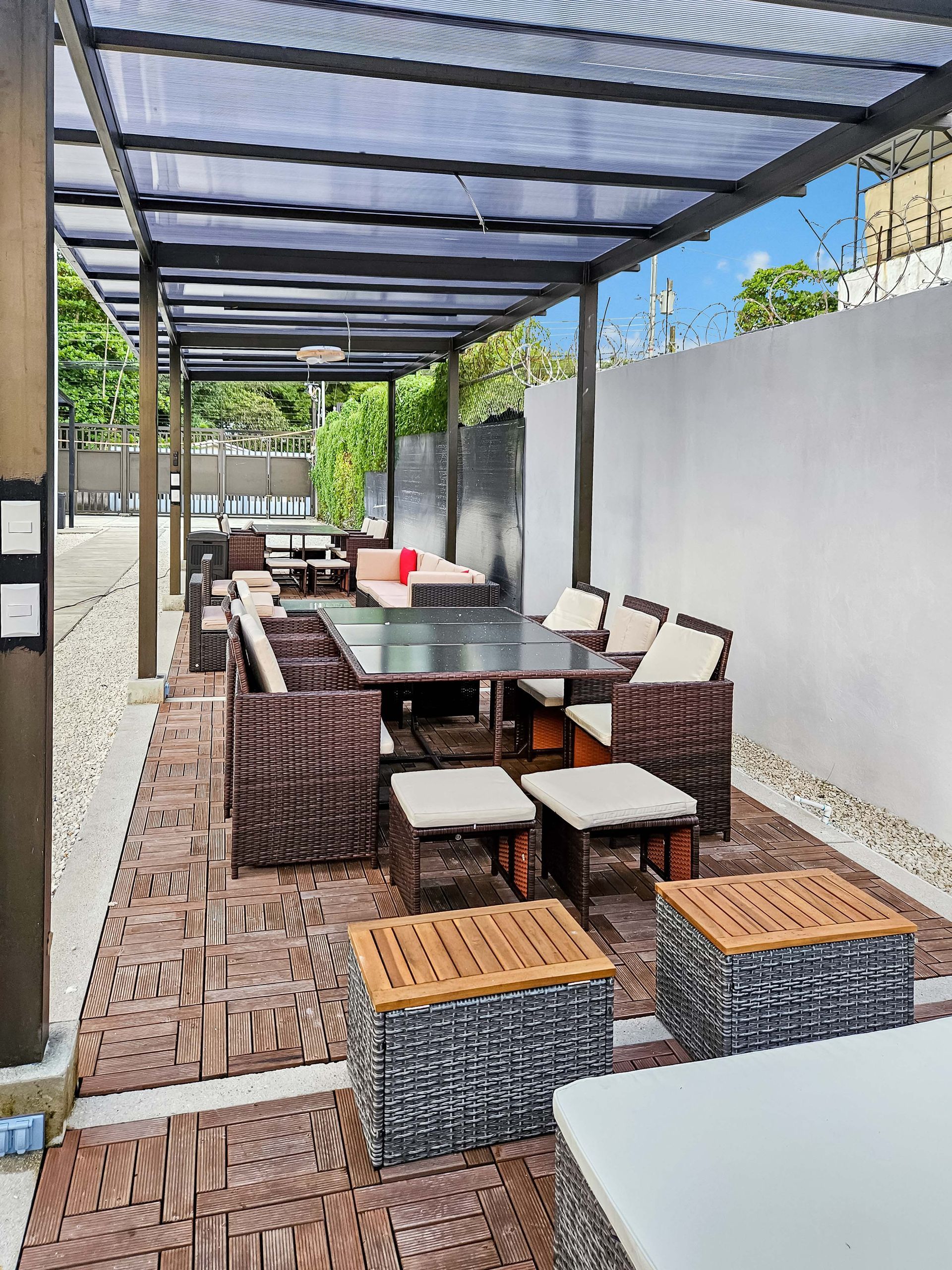 Outdoor dining area with a long table, wicker chairs, and a pergola.