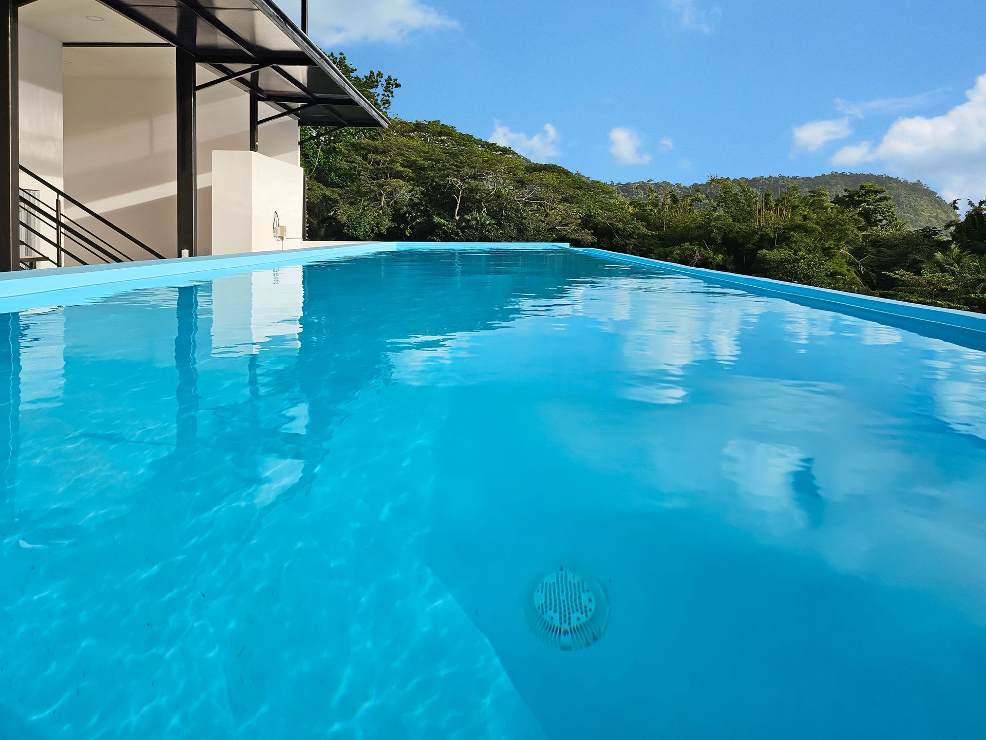 Blue infinity pool overlooking lush greenery under a blue sky.