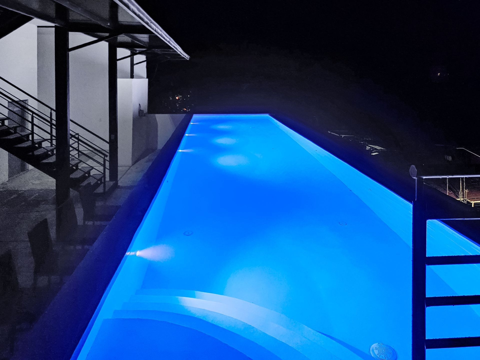 Illuminated blue infinity pool at night, modern architecture.