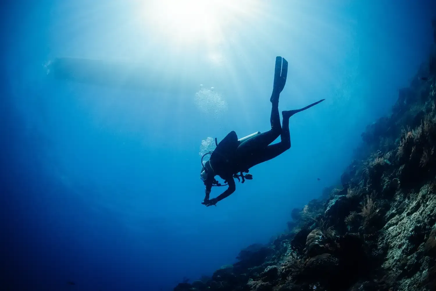 Scuba diver descends in deep blue water, sun rays beaming from above.